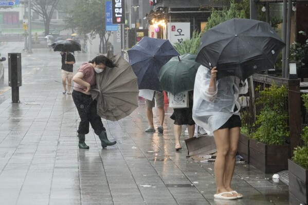 People struggle to hold onto their umbrellas in the rain and wind as the tropical storm named Khanun approaches to the Korean Peninsular, in Busan, Thursday, Aug. 10, 2023. (AP Photo/Ahn Young-joon)