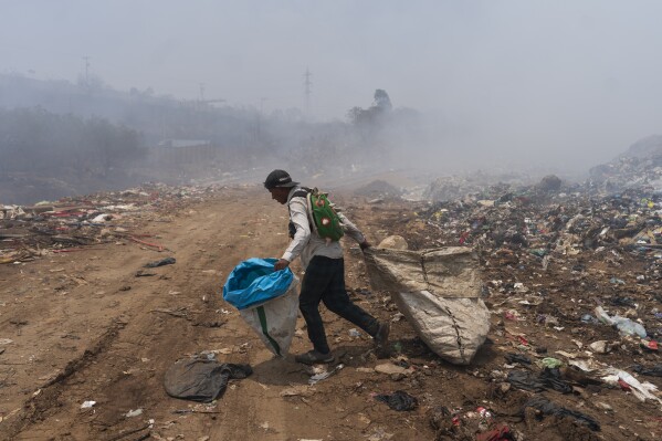 A waste picker walks past clouds of smoke generated by a fire at a garbage dump in Villa Nueva, Guatemala, Tuesday, April 9, 2024. According to the Guatemalan emergency agency CONRED, 60 percent of the fire has been controlled as the poor air quality in the country's capital caused schools to close for two days. (AP Photo/Moises Castillo)