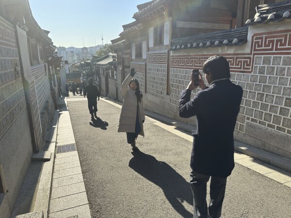Tourists wander taking photos of the residential neighborhood and its many restored traditional houses in the Bukchon Hanok Village, in Seoul, Wednesday, Dec. 4, 2024. (AP Photo/ Jennifer McDermott)