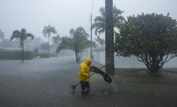 on Wednesday, June 12, 2024, in Hollywood, Fla.  (Matthias J. Ochner/Miami Herald via AP) A man works to clear debris from a flooded street after heavy rains hit parts of South Florida.