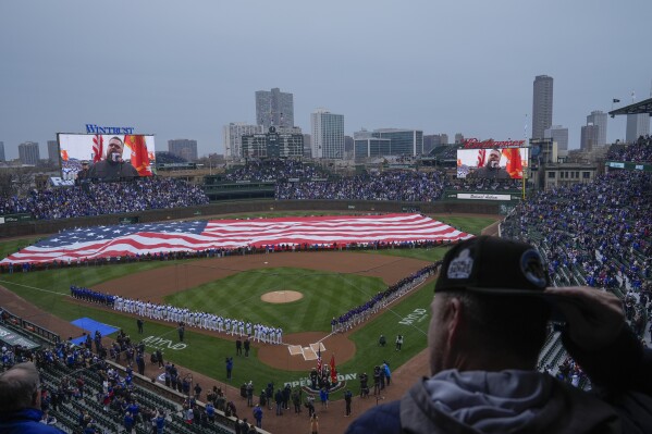 A large American flag is displayed during the Star-Spangled Banner before an opening day baseball game between the Colorado Rockies and Chicago Cubs, Monday, April 1, 2024, in Chicago. (AP Photo/Erin Hooley)
