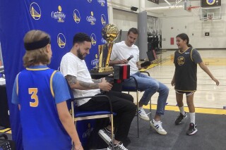Golden State Warriors youth campers Will McCloskey, left, and Amari Chiefelk, right, present former Warriors players Nemanja Bjelica and Chris Chiozza, second from left, with their 2022 NBA championship rings in a special ceremony, Wednesday, July 19, 2023, in Oakland, Calif. Typically, the Warriors present former players with their rings in a pregame on-court ceremony when they come through town with an opposing organization, but these two were playing overseas. (AP Photo/Janie McCauley)