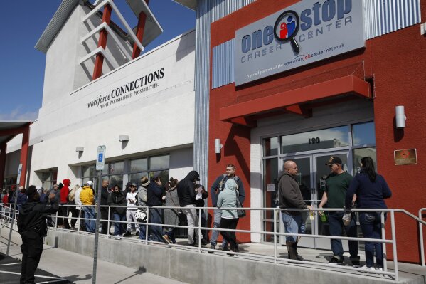 FILE - In this March 17, 2020 file photo, people wait in line for help with unemployment benefits at the One-Stop Career Center in Las Vegas.  More than 6.6 million Americans applied for unemployment benefits last week of March 23, far exceeding a record high set just last week, a sign that layoffs are accelerating in the midst of the coronavirus.  (AP Photo/John Locher, File)