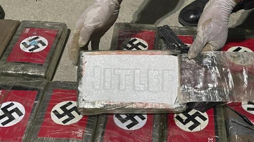 In this photo provided by the Peruvian Anti-Drug Police, an officer shows blocks of cocaine marked with Nazi swastikas and stamped with the name 