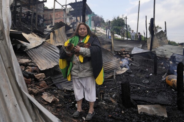 Veronica Kutdo stands with salvaged hens amid the charred debris of her home after an overnight fire in Bogota, Colombia, Friday, March 8, 2024. (AP Photo/Fernando Vergara)