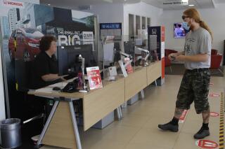 FILE - A customer wearing a face mask to protect against coronavirus, social distances in the car servicing department at the Trident Honda car dealership in Ottershaw, England, Friday, May 29, 2020. A new car warranty is a contract between the automaker and the vehicle owner. But if the owner doesn’t hold up his or her part of the bargain, it could void all the coverage. Here are a few reasons why your warranty claim can be denied and tips on how to avoid any issues down the road. (AP Photo/Kirsty Wigglesworth)