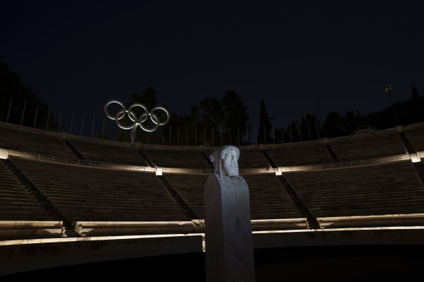 The Olympic rings are seen behind the double face marble statue known as Hermes in the marble Panathinean Stadium, venue of the first modern Olympics in 1896, in Athens, early Friday, April 5, 2024. (AP Photo/Petros Giannakouris)