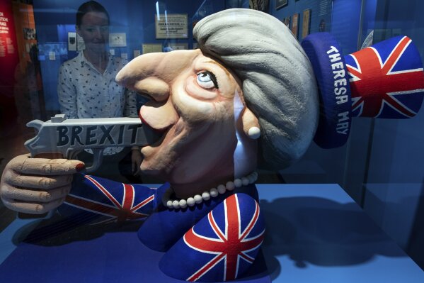 FILE - In this Tuesday July 9, 2019 file photo a woman looks to a model of a carnival float from Duesseldorf depicting British Prime Minister Theresa May and the Brexit at the exhibition 'Very British' about the Germany- Britain relationship at the German House Of History museum in Bonn, Germany. (Federico Gambarini/dpa via AP, file)