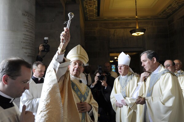 档案-2012年5月16日，康涅狄格州布里奇波特教区前主教、大主教威廉·E·洛里在巴尔的摩玛丽女王大教堂举行弥撒时，在被任命为巴尔的摩第16任大主教之前，向圣水洒水。根据2024年5月22日（星期三）发布的最终计划，巴尔的摩天主教大主教管区将把该市及其附近郊区的教区数量减少约三分之二，这是针对出勤率下降和基础设施老化的重新调整计划的一部分。据《巴尔的摩太阳报》报道，大主教洛里表示，四次市政厅会议对该计划草案的反馈至关重要。（美联社照片/Steve Ruark，档案）