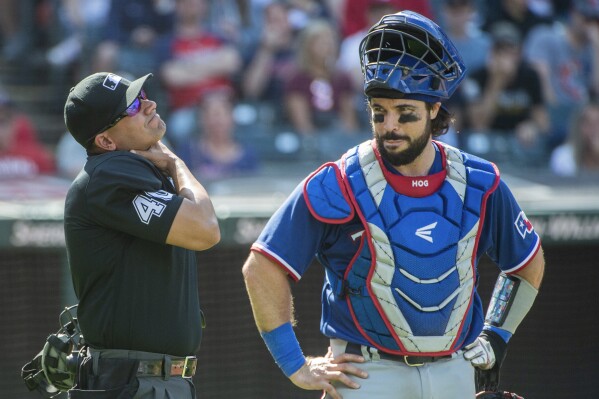 FILE - Umpire Roberto Ortiz, left, holds his neck after being hit by a foul ball by Cleveland Guardians' Ramon Laureano (not shown) as Texas Rangers' Austin Hedges, right, looks on during the fourth inning of a baseball game in Cleveland, Sept. 17, 2023. The Guardians are reuniting with Hedges, agreeing with the veteran catcher on a one-year, $4 million contract, a person familiar with the deal told The Associated Press, Sunday, Dec. 10, 2023. (AP Photo/Phil Long, File)