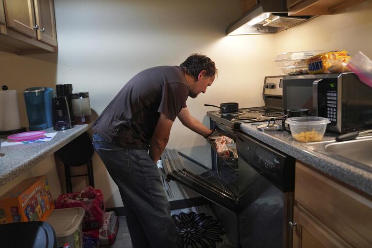 Andrew Hackney cooks dinner for his 1-year-old daughter during a supervised visit at his and his wife's apartment in Oakdale, Pa., on Thursday, Nov. 17, 2022. Andrew, 33, has a comprehension disorder and nerve damage from a stroke suffered in his 20s. (AP Photo/Jessie Wardarski)