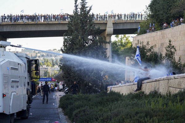 Israeli police use a water cannon to disperse demonstrators blocking a road during a protest against plans by Prime Minister Benjamin Netanyahu's government to overhaul the judicial system, in Jerusalem, Monday, July 24, 2023. Israeli lawmakers on Monday approved a key portion of Prime Minister Benjamin Netanyahu's divisive plan to reshape the country's justice system despite massive protests that have exposed unprecedented fissures in Israeli society. (AP Photo/Ohad Zwigenberg)