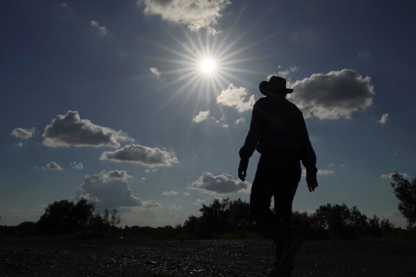 FILE - Jessie Fuentes, who works providing people with canoes and kayaks, walks along the Rio Grande with the sun pushing the temperature into the 90s on July 6, 2023. The death certificates of more than 2,300 people who died in the United States last summer mention the effects of excessive heat, the highest number in 45 years of records, according to an Associated Press analysis of Centers for Disease Control and Prevention data. With May already breaking heat records, 2024 could be even deadlier. (AP Photo/Eric Gay, File)
