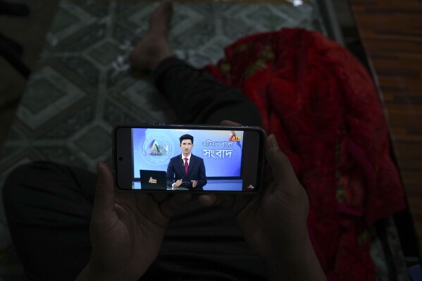 A Bangladeshi migrant worker watches Bangladeshi news on his phoneat a dormitory in Klang, Malaysia, Friday, Jan. 24, 2025. (AP Photo/Azneal Ishak).