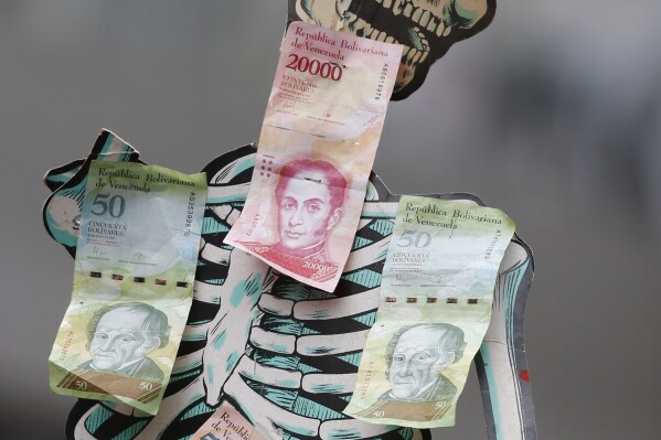 FILE - A skeleton is adorned with Venezuelan Bolivar bills to draw attention to the devaluation of the currency and hunger, during an opposition march in Caracas, Venezuela, March 10, 2020. (AP Photo/Ariana Cubillos, File)