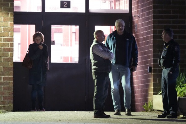 People stand outside a reunification center early Thursday, Oct. 26, 2023, at Auburn Middle School in Auburn, Maine, after shootings Wednesday at a bar and a bowling alley in Lewiston, Maine. (AP Photo/Steven Senne)