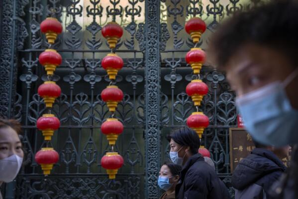 People wearing face masks walk past rows of lanterns at a tourist shopping street in Beijing, Tuesday, Feb. 28, 2023. (AP Photo/Mark Schiefelbein)