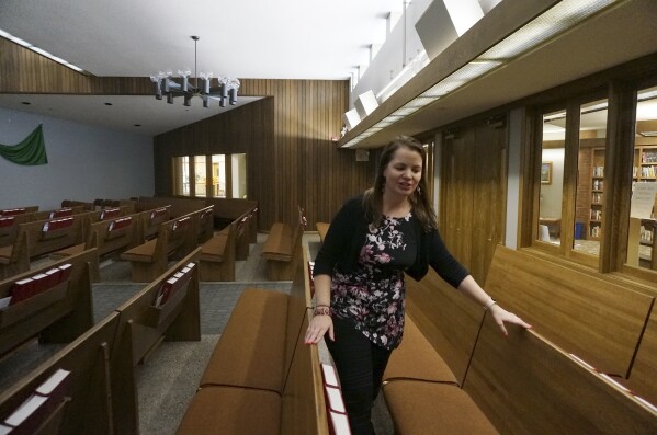 The Rev. Karna Moskalik walks through each line of pews in the sanctuary of Our Savior's Lutheran Church in Stillwater, Minn., on Wednesday Sept. 27, 2023. Lighting a perfumed candle, praying, and meditating are all strategies she employs to ground her and be a more effective faith leader after doing doctoral research on resiliency. (AP Photo/Giovanna Dell'Orto)
