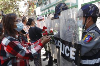 Supporters give roses to police while four arrested activists make a court appearance in Mandalay, Myanmar, Friday, Feb. 5, 2021. Hundreds of students and teachers have taken to Myanmar's streets to demand the military hand power back to elected politicians, as resistance to a coup swelled with demonstrations in several parts of the country. (AP Photo)