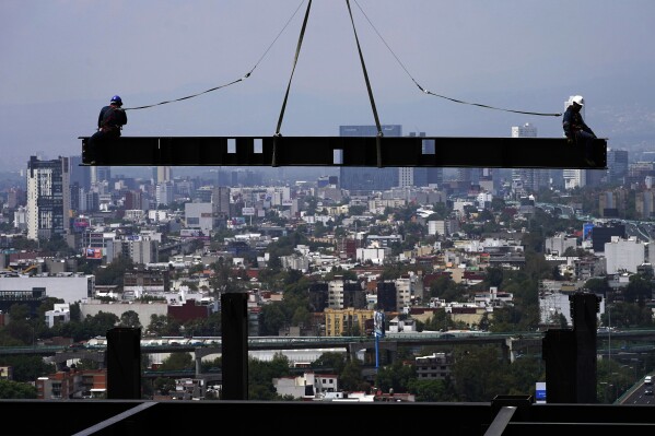 FILE - Construction workers ride on a beam hanging from a crane at the construction site of a residential high rise building in Mexico City, June 17, 2022. Mexico's economy barely eked out a 0.1% increase in the fourth quarter, bringing estimated growth for 2023 to 3.1%, according to preliminary figures published Tuesday, Jan. 30. 2024, by Mexico’s National Statistics Institute. (AP Photo/Marco Ugarte, File)