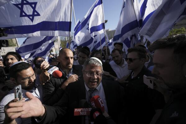 FILE - Israeli lawmaker Itamar Ben-Gvir, center, surrounded by right wing activists with Israeli flags, speaks to the media as they gather for a march in Jerusalem, Wednesday, April 20, 2022. Ben-Gvir, an ultranationalist lawmaker who was once relegated to the margins of Israeli politics, is surging in the polls ahead of November’s parliamentary elections. (AP Photo/Ariel Schalit, File)