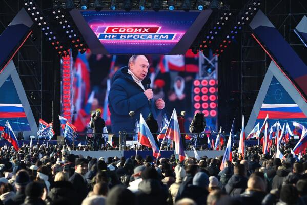 Russian President Vladimir Putin seen on the big screen as he delivers his speech at the concert marking the eighth anniversary of the referendum on the state status of Crimea and Sevastopol and its reunification with Russia, in Moscow, Russia, Friday, March 18, 2022, with a banner reading "For Russia" projected in the backgroud. (Vladimir Astapkovich/Sputnik Pool Photo via AP)