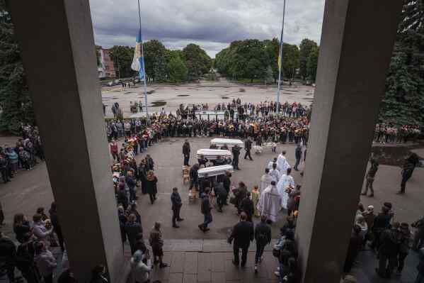 Funeral workers carry coffins during a funeral ceremony for Tamara Martyniuk, 8, Stanislav Martyniuk, 12, and Roman Martyniuk, 17, killed in a Russian strike on Sunday, in Korostyshiv, Zhytomyr region, Ukraine, Wednesday, May 28, 2025. (AP Photo/Evgeniy Maloletka)
