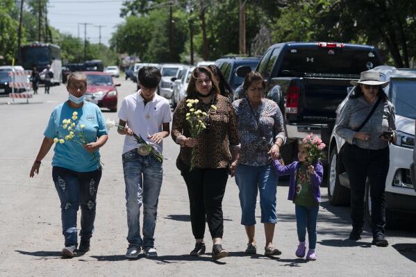 People walk with flowers to honor the victims in Tuesday's shooting at Robb Elementary School in Uvalde, Texas, Wednesday, May 25, 2022. Desperation turned to heart-wrenching sorrow for families of grade schoolers killed after an 18-year-old gunman barricaded himself in their Texas classroom and began shooting, killing at least 19 fourth-graders and their two teachers. (AP Photo/Jae C. Hong)