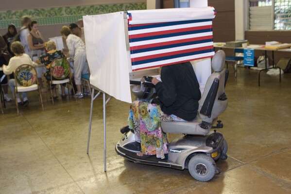 FILE - A woman in a motorized wheelchair casts her vote at the Waikiki Community Center in Honolulu, on Tuesday, Nov. 4 2008. (AP Photo/Marco Garcia, File)