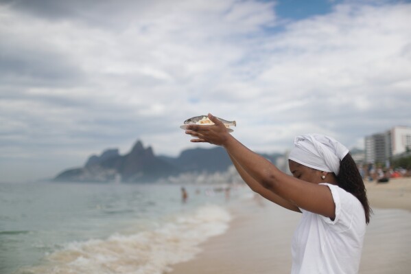 A devotee raises a fish as an offering during an annual celebration honoring Yemanja, the African goddess of the sea, at Arpoador Beach in Rio de Janeiro, Sunday, Feb. 2, 2025. (AP Photo/Bruna Prado)