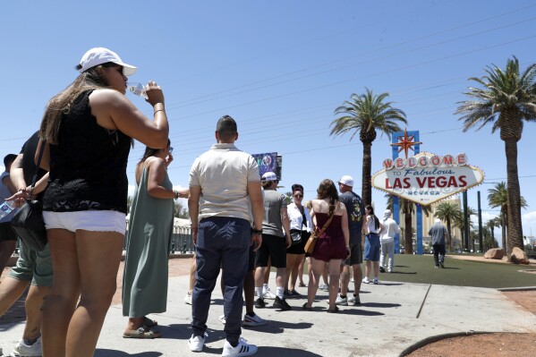 Sofía Ramírez, izquierda, de México bebe agua mientras espera en la fila para tomarse una foto en el letrero Welcome to Fabulous Las Vegas en Las Vegas el jueves 6 de junio de 2024. (Steve Marcus/Las Vegas Sun via AP)