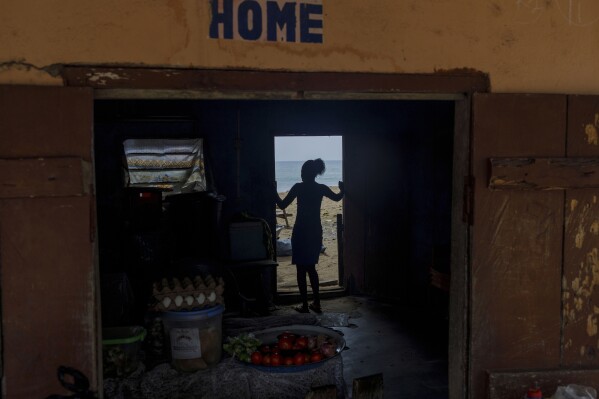 Afeli Bernice Adzo stands at the entrance of the remains of her father's 10-unit family home in Avegadzi, Ghana, Wednesday, March 5, 2025 (AP Photo/Misper Apawu)