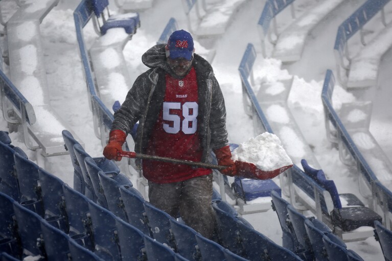A worker helps clear snow from Highmark Stadium in Orchard Park, New York, Sunday, Jan. 14, 2024. A potentially dangerous snowstorm that hit the Buffalo area on Saturday led the NFL to postpone the Bills' Wild Card game against the Pittsburgh Steelers from Sunday to Monday.  New York Governor Kathy Hochul and the NFL cited public safety concerns for the postponement, as up to two feet of snow is expected to fall on the area over a 24-hour period.  (AP Photo/Jeffrey T. Barnes)