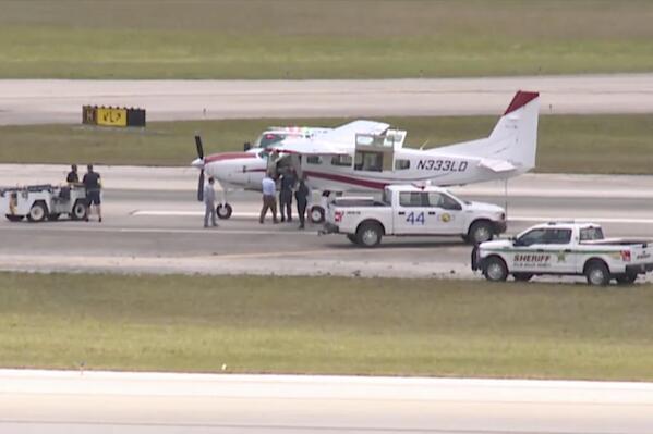 In this still image from video by WPTV shows emergency personnel surrounding a Cessna plane at Palm Beach International Airport Tuesday, May 10, 2022, in West Palm Beach, Fla. A passenger with no flying experience was able to land the plane safely with help of air traffic controllers after the pilot was too sick to handle the controls. (WPTV via AP)