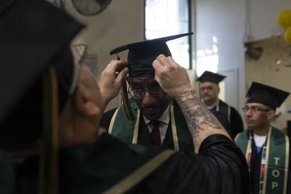Prisoner-student Gabriel Bonilla adjusts a cap for Michael Love, center, while waiting for the start of their graduation ceremony at Folsom State Prison in Folsom, Calif., Thursday, May 25, 2023. After serving more than 35 years in prison, Love is currently enrolled in a Master's program at Sacramento State. He is employed by Project Rebound, an organization that assists and mentors formerly incarcerated people as they further their education. Love has also been hired as a teaching aide and will teach freshmen communications students in the fall. (AP Photo/Jae C. Hong)