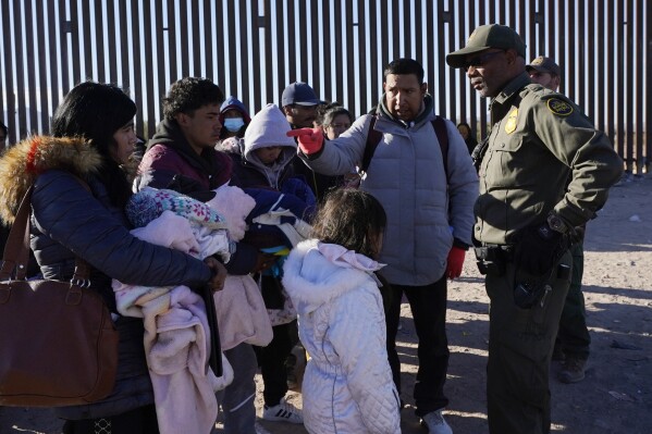 Luiz Velazquez, second from right, from Zacatecas, Mexico, points to his family as he talks with a member of the U.S. Border Patrol as they gather at the border in Lukeville, Ariz., Tuesday, Dec. 5, 2023 Join hundreds of would-be migrants.  (AP Photo/Ross D. Franklin)