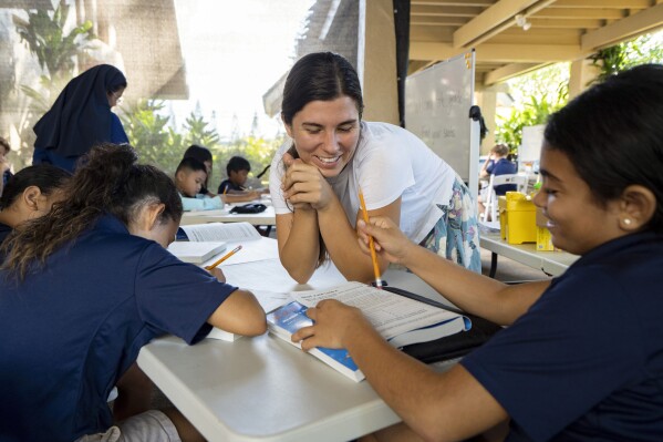 Sacred Hearts School second grade teacher Courtney Copriviza interacts with the fourth graders at their temporary school site at Sacred Hearts Mission Church on Tuesday, Oct. 3, 2023, in Lahaina, Hawaii. Sacred Hearts and other private schools across the state took in displaced public school students, and offered a year of free tuition. (AP Photo/Mengshin Lin)