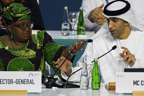 Emirati Minister of State for Foreign Trade Thani bin Ahmed al-Zeyoudi, right, prepares to speak into a microphone provided by World Trade Organization Director-General Ngozi Okonjo-Iweala at a WTO summit in Abu Dhabi, United Arab Emirates, Monday, Feb. 26, 2024. The World Trade Organization opened its biennial meeting Monday in the United Arab Emirates as the bloc faces pressure from the United States and other nations ahead of a year of consequential elections around the globe. (AP Photo/Jon Gambrell)