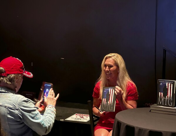 U.S. Rep. Marjorie Taylor Greene, R-Ga., poses with a copy of her book on Saturday, May 18, 2024, at the Georgia Republican Party Convention in Columbus, Ga. (AP Photo/Jeff Amy)