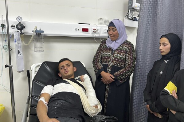 Al-Amur sits in a hospital bed next to his relatives following an attack by Israeli settlers on his West Bank village of Jinba, Friday, March 28, 2025. (Basel Adra via AP)