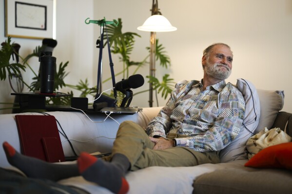 Michael Bommer, who is terminally ill with colon cancer, smiles as he sits on his sofa during a meeting with The Associated Press at his home in Berlin, Germany, Wednesday, May 22, 2024. Bommer, who has only a few more weeks to live, teamed up with friend who runs the AI-powered legacy platform Eternos to "create a comprehensive, interactive AI version of himself, allowing relatives to engage with his life experiences and insights," after he has passed away. (AP Photo/Markus Schreiber)
