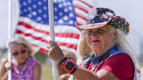 FILE - Supporters wave flags as they wait for the motorcade of former President Donald Trump to arrive at Palm Beach International Airport in West Palm Beach, Fla., March 25, 2023. Millions of Americans will attend parades, fireworks, barbecues and other Independence Day events on Tuesday, celebrating the courage and sacrifices of the nation’s 18th century patriots who fought for the nation’s independence from England and what they considered an unjust government. (AP Photo/Gerald Herbert, File)