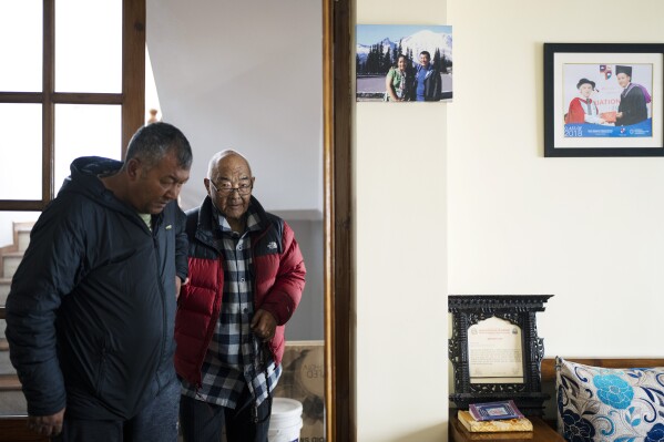 Kanchha Sherpa, right, is helped by his son Tsering Sherpa before an interview with Associated Press at his residence in Kathmandu, Nepal, Saturday, March 2, 2024. (AP Photo/Niranjan Shrestha)