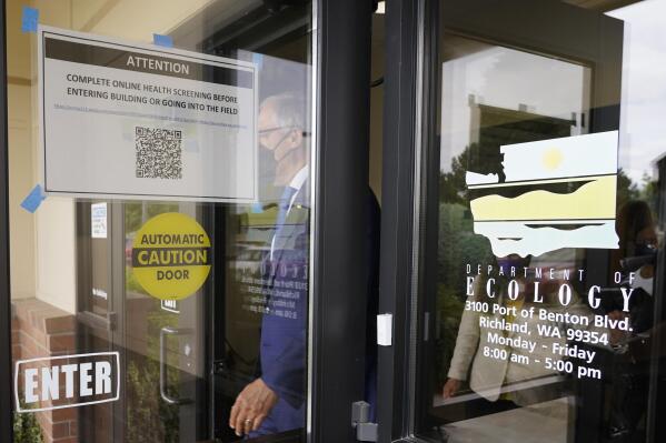 Washington Gov. Jay Inslee walks past a sign asking visitors to complete a health screening as he steps outside to talk to reporters, Thursday, June 2, 2022, at a Dept. of Ecology office in Richland, Wash. On May 25, 2022, Inslee's office said the Governor had tested positive for COVID-19. Inslee, who has recently criticized the slow pace of cleaning up the Hanford Nuclear Reservation in Washington state, was speaking ahead of a scheduled tour of the nuclear weapons production site and repeated his message that more federal money is needed to finish the job. (AP Photo/Ted S. Warren)