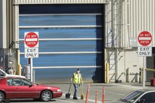 FILE - In this April 13, 2020 file photo, a worker wears a mask as he cleans up an area outside an entrance at Boeing Co.'s airplane assembly facility in Everett, Wash., north of Seattle. American industry collapsed in March as the coronavirus pandemic wreaked havoc on the U.S. economy. Manufacturing and overall industrial production posted the biggest drops since the United States demobilized after World War II. (AP Photo/Ted S. Warren, File)
