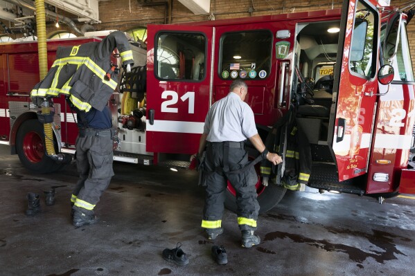 Firefighter Rod MacKinnon, left, and Lt. Chris Stevens don their turnout gear as they respond to a call at the Engine 21 fire station, Thursday, Aug. 24, 2023, in the Dorchester neighborhood of Boston. (AP Photo/Michael Dwyer)