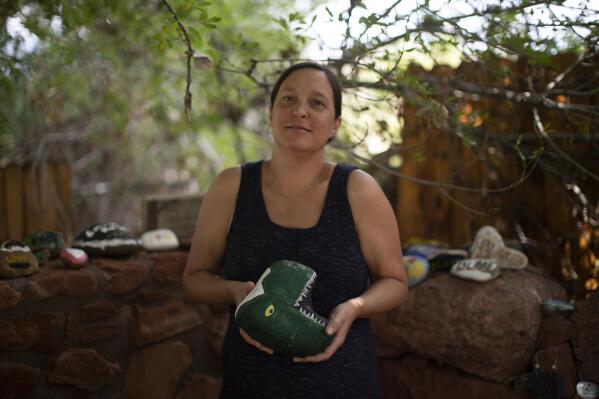 Liz Castleman holds up a rock with a dinosaur painted on it to honor her son Charlie, at the Selah Carefarm in Cornville, Ariz., Oct. 4, 2022. "All of the old safe spaces are gone. The farm, it really is the one safe space," says 46-year-old Castleman, whose son died while under anesthesia during an MRI, likely due to an underlying genetic disorder. "There's something, I don't know if it's magical, but you know that anything you say is OK and anything you feel is OK. It's just a complete bubble from the rest of the world." (AP Photo/Dario Lopez-Mills)