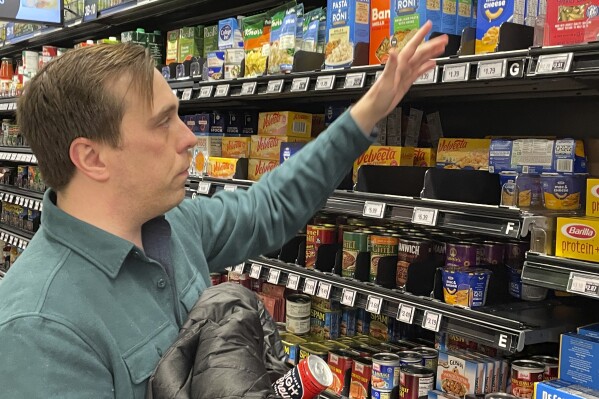 Stuart Dryden reaches for an item at a grocery store on Wednesday, Feb. 21, 2024, in Arlington, Va. Dryden is aware of big price disparities between branded products and their store-label competitors, which he now favors. (AP Photo/Chris Rugaber)