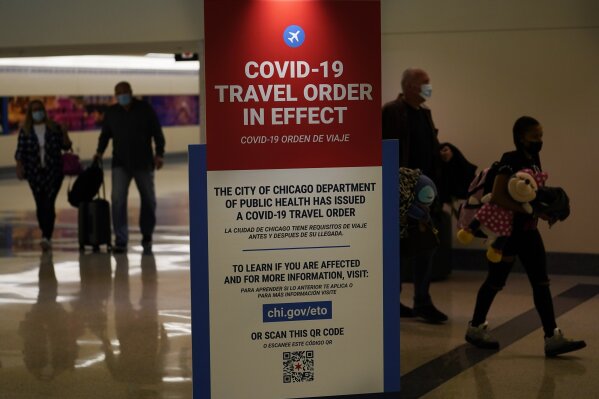 FILE - In this Nov. 24, 2020 file photo, air travelers arriving at Midway Airport in Chicago are reminded of the city's COVID-19 travel orders. More than 1 million people have passed through U.S. airport security checkpoints in each of the past two days in a sign that public health pleas to avoid holiday travel are being ignored, despite an alarming surge in COVID-19 cases. (AP Photo/Charles Rex Arbogast, File)