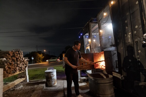 Miguel Vidal feeds the fire while smoking ribs and brisket in the middle of the night at his restaurant, Valentina's Tex Mex BBQ, early Saturday, April 22, 2023, in Austin, Texas. Later in the year, the restaurant re-opened in Buda, a suburb south of the capital. "As far back as I can remember, every get together we had was at my grandmother's house and my uncle's house. And it was always around fire, always around either grilling or smoking or barbecues," said Vidal. "So to me, that's how I grew up eating. That's just like what it was. Food brings people together, and it's really important to be able to share that." (AP Photo/David Goldman)
